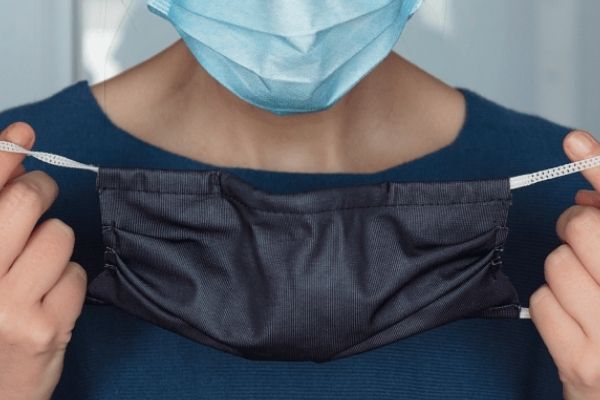 A woman wearing a surgical mask is holding up a fabric mask to double mask with