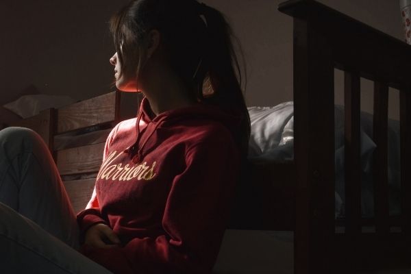 A girl sitting alone in a dark room and looking out the window