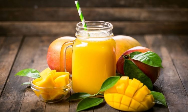 Mango Drink Recipes: A mason jar with a mango drink surrounded by whole and cut mangoes