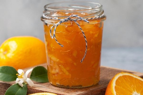 A jar of orange marmalade jam kept on a wooden slab