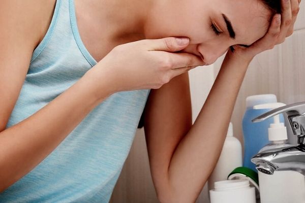 A woman feeling nauseous and leaning over the sink with her hand on her mouth