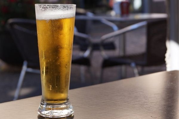 A beer glass kept on a table with two chairs in the background