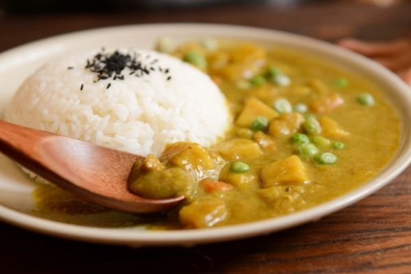 A portion of white rice served with some potatoes and peas curry on a cream coloured plate